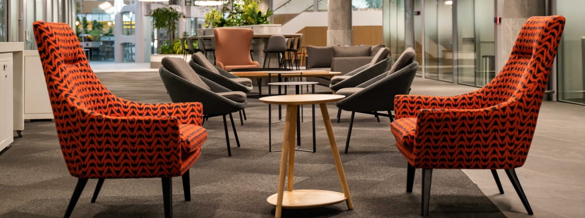 A waiting area with burnt orange armchairs and charcoal seats with small tables.
