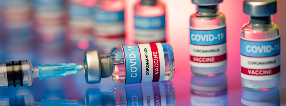 Multiple COVID-19 vaccine bottles with one laying on its side with a syringe inserted.